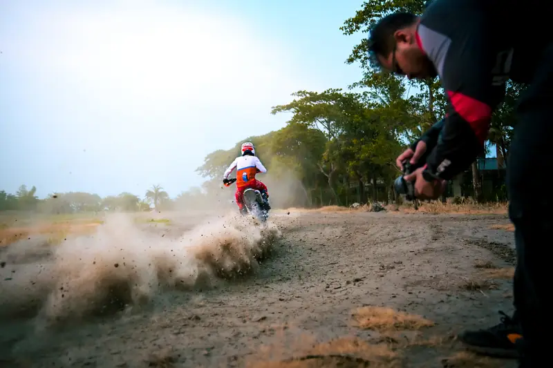 Photographer crouched trackside as a dirt bike roosts past