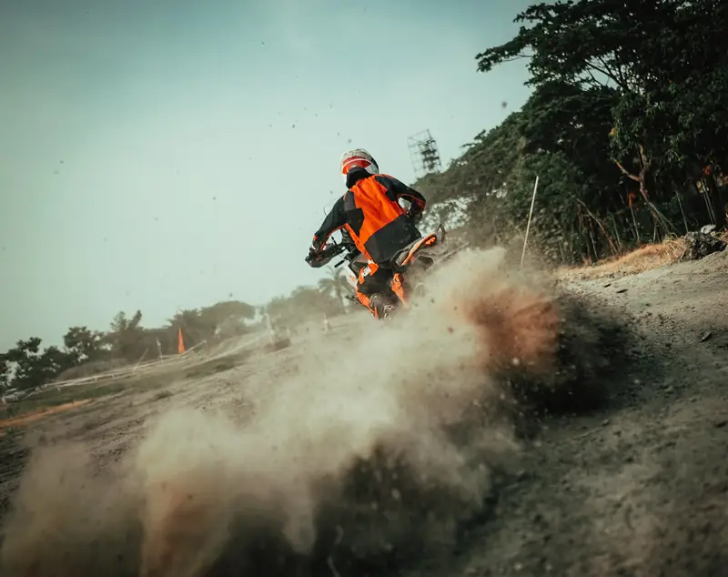 Rider powering up a dusty bank, dirt spraying from the rear wheel