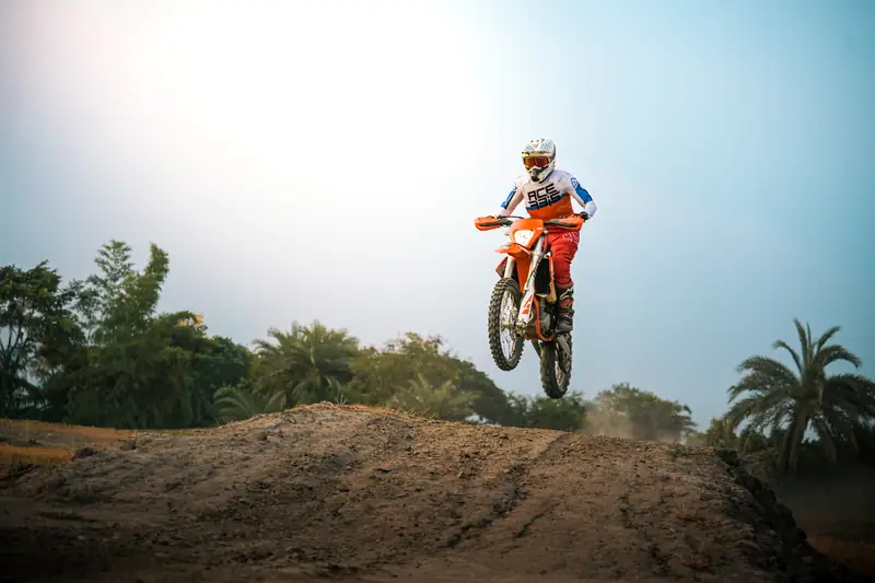 Rider airborne over a dirt jump against a bright sky