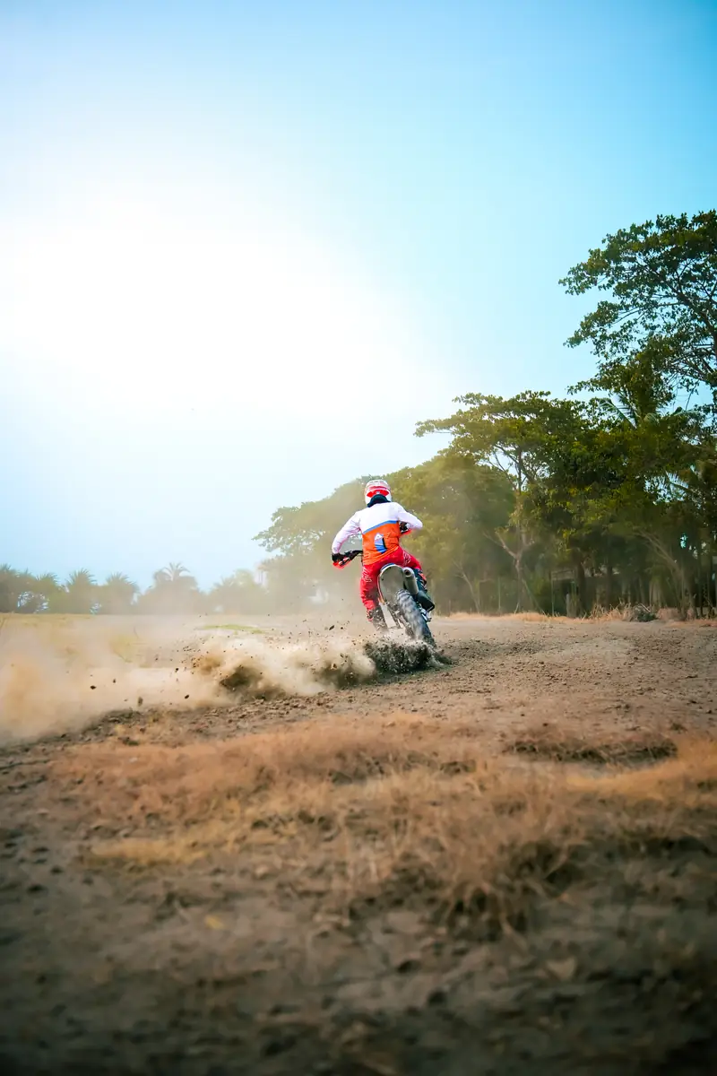 Dirt bike kicking up dust on an open track lined with trees