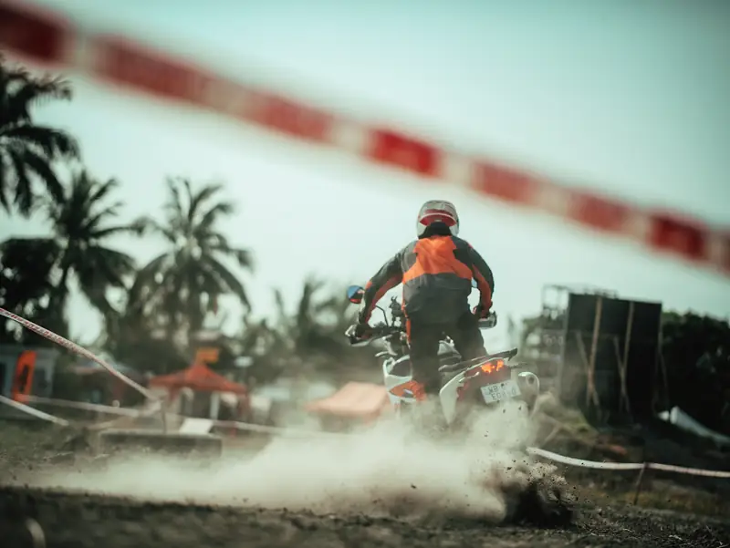 Rider accelerating away past course tape, dust flying