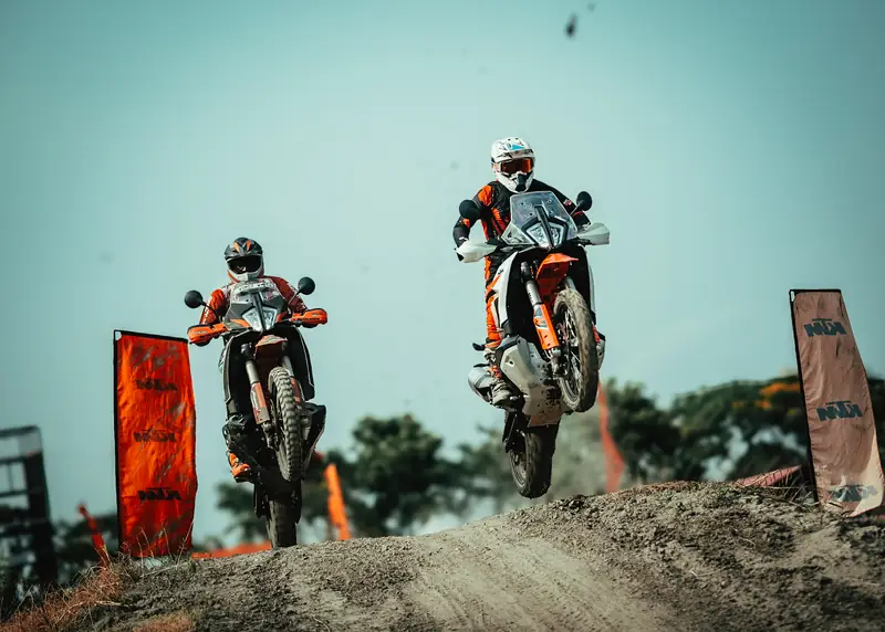 Two adventure motorcycles taking off over a jump